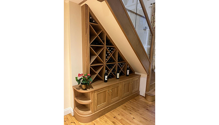 This bespoke under stairs oak wine rack designed by Simon Taylor cleverly includes cupboards to store games and consoles, and the extended curved cabinet end with open shelving finished with skirting makes it a stylish addition