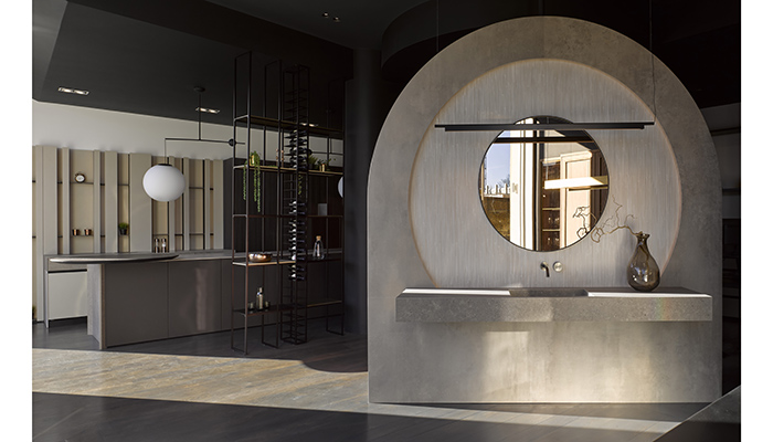 Bathroom display featuring Atlasplan Habitat Boost Stone Taupe porcelain basin and wall panel, with Novocastrian Port Round Blackened Steel bronze tint mirror and Luceplan Compendium suspended LED black pendant light