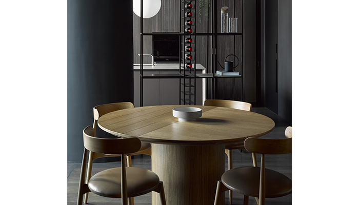 L’Ottocento Meridiana table and Ottavia chairs, both in Rovere Chiara (Light Oak), in front of The Cut Yugen black powder coated steel framed shelving system, used as a room divider